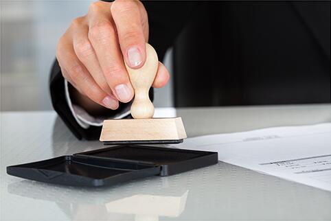 Hand with a stamp on a stamp pad and a document next to the hand.